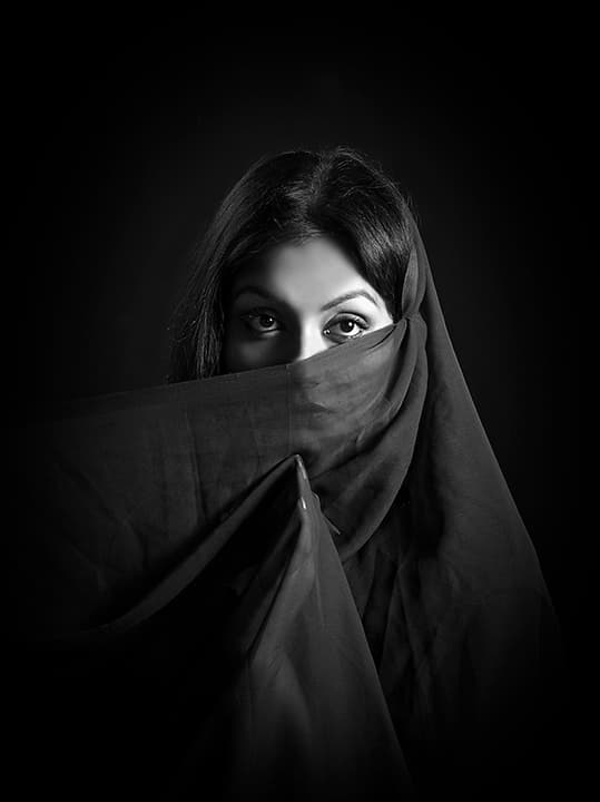 Eyes over a dark chiffon veil drawn up by an unseen hand