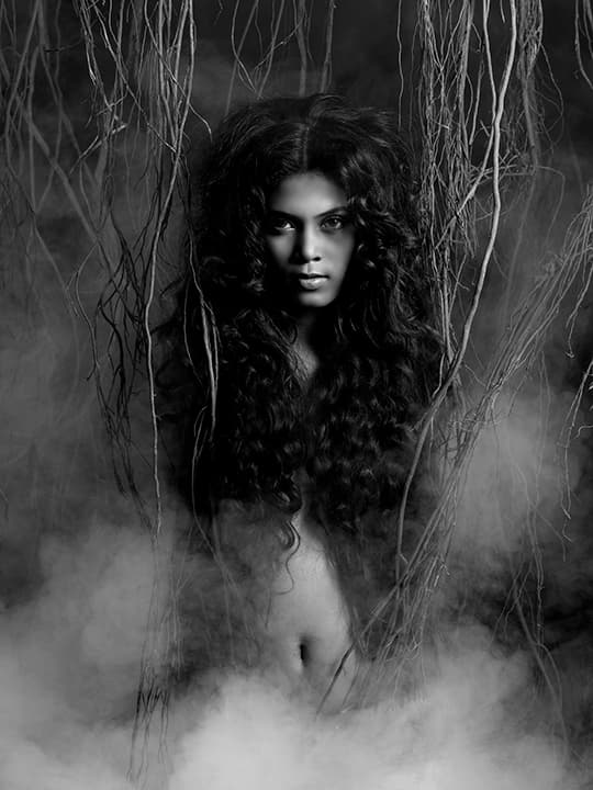 Wild-haired figure rising out of fog among hanging roots